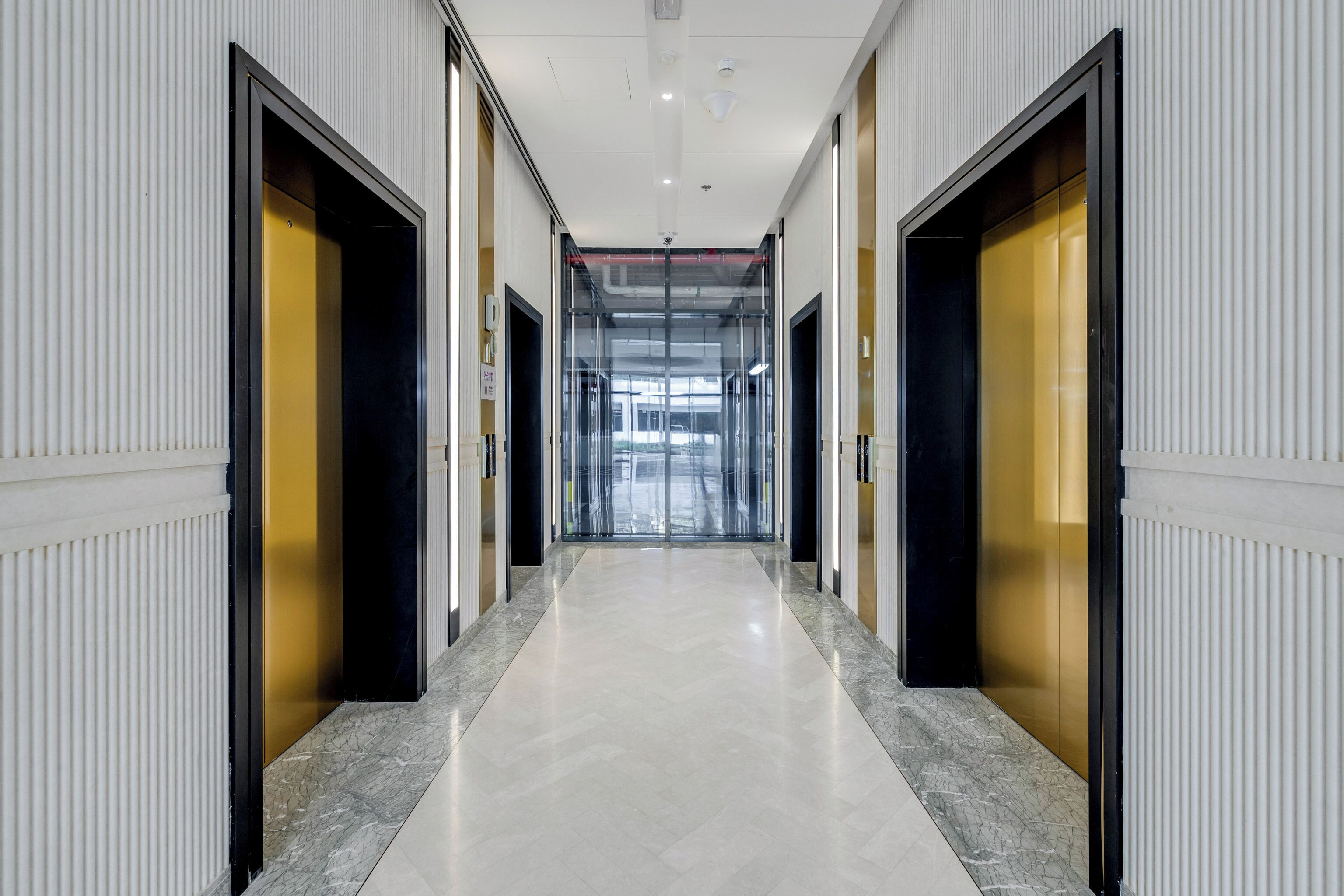 A corridor with doors on both sides, leading to a glass elevator area.