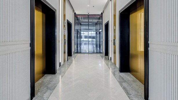 A corridor with doors on both sides, leading to a glass elevator area. - GlobalStay Azizi Riviera 42 (Dubai)