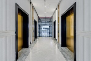 Un pasillo con puertas a ambos lados que conduce a una zona con ascensor de vidrio.