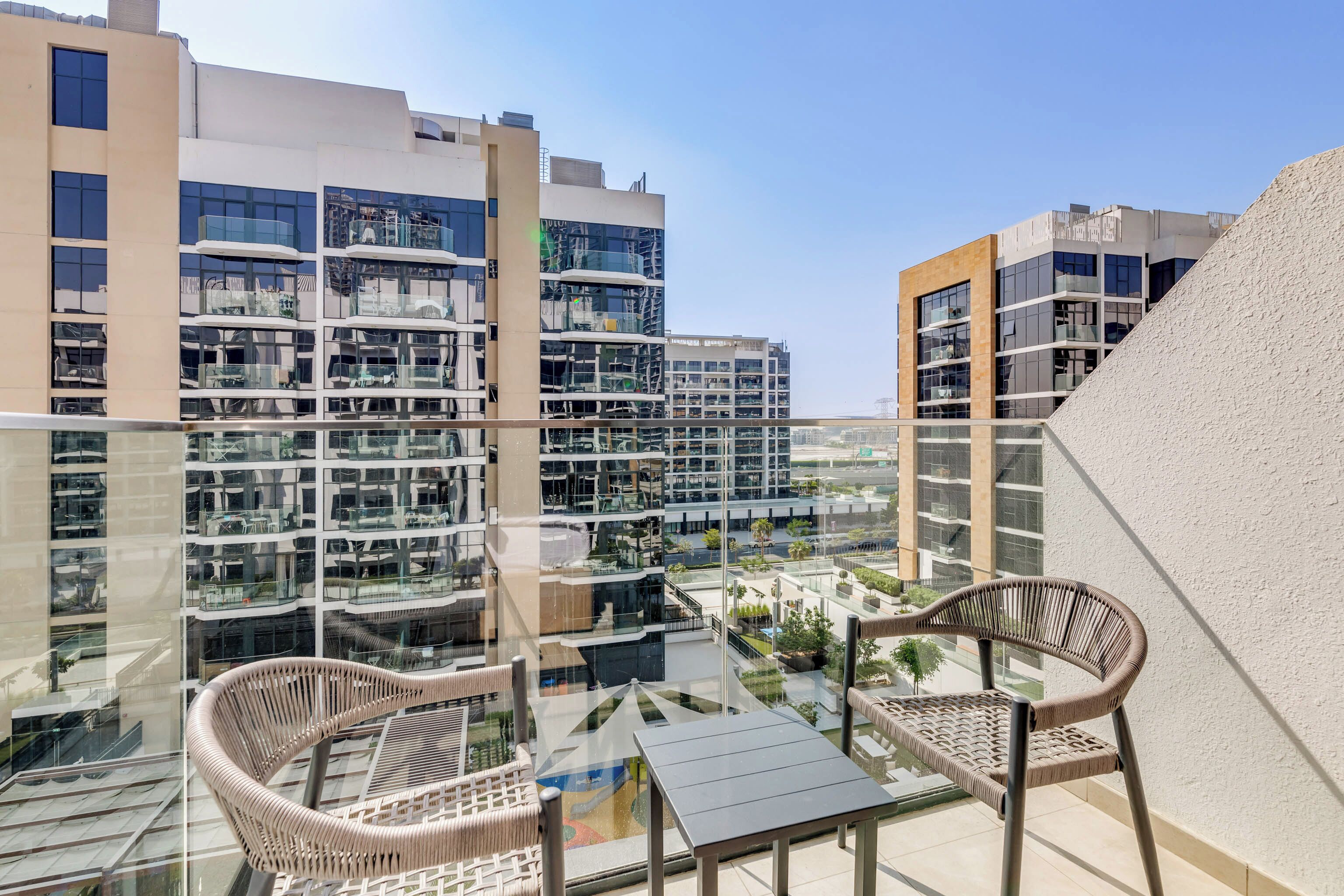 Eine moderne Wohnung mit Balkon, möbliert mit Korbstühlen und einem Glastisch, mit Blick auf eine Skyline mit Hochhäusern.