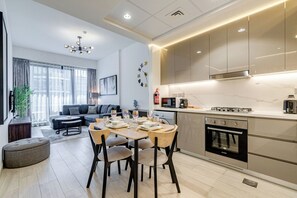 Una sala de estar moderna con sofá, mesa de comedor y sillas, una cocina equipada y un ventanal con cortinas.