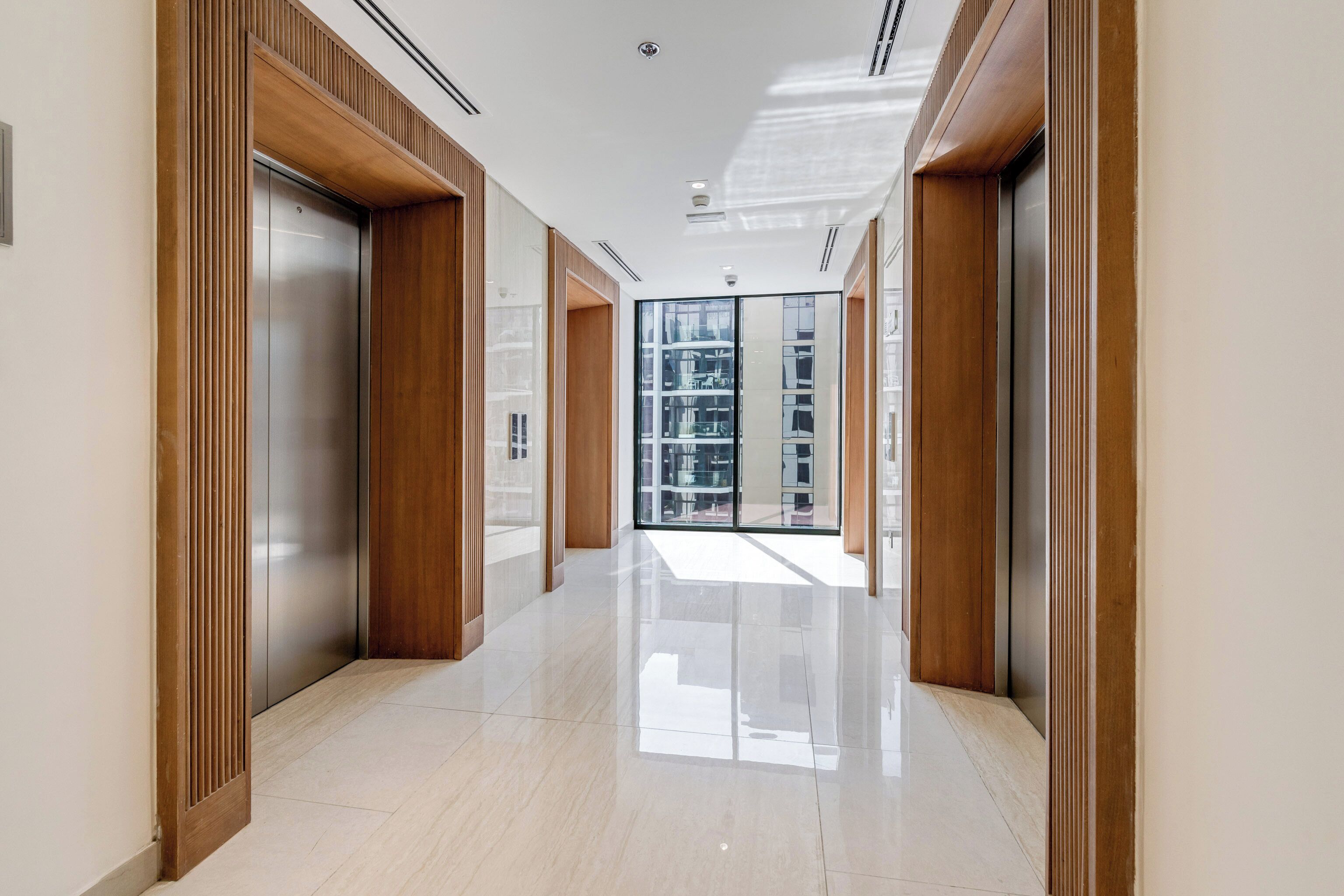 A modern hallway with elevators and glass doors leading to a commercial space.