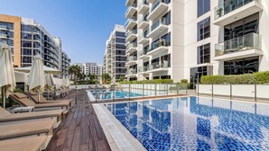 A modern residential building with a rooftop swimming pool, lounge chairs, and a clear sky. - GlobalStay Azizi Riviera 42 (Dubai)