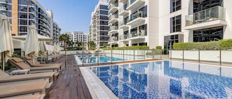 Un immeuble résidentiel moderne doté d’une piscine sur le toit, de chaises longues et offrant une vue sur un ciel dégagé.