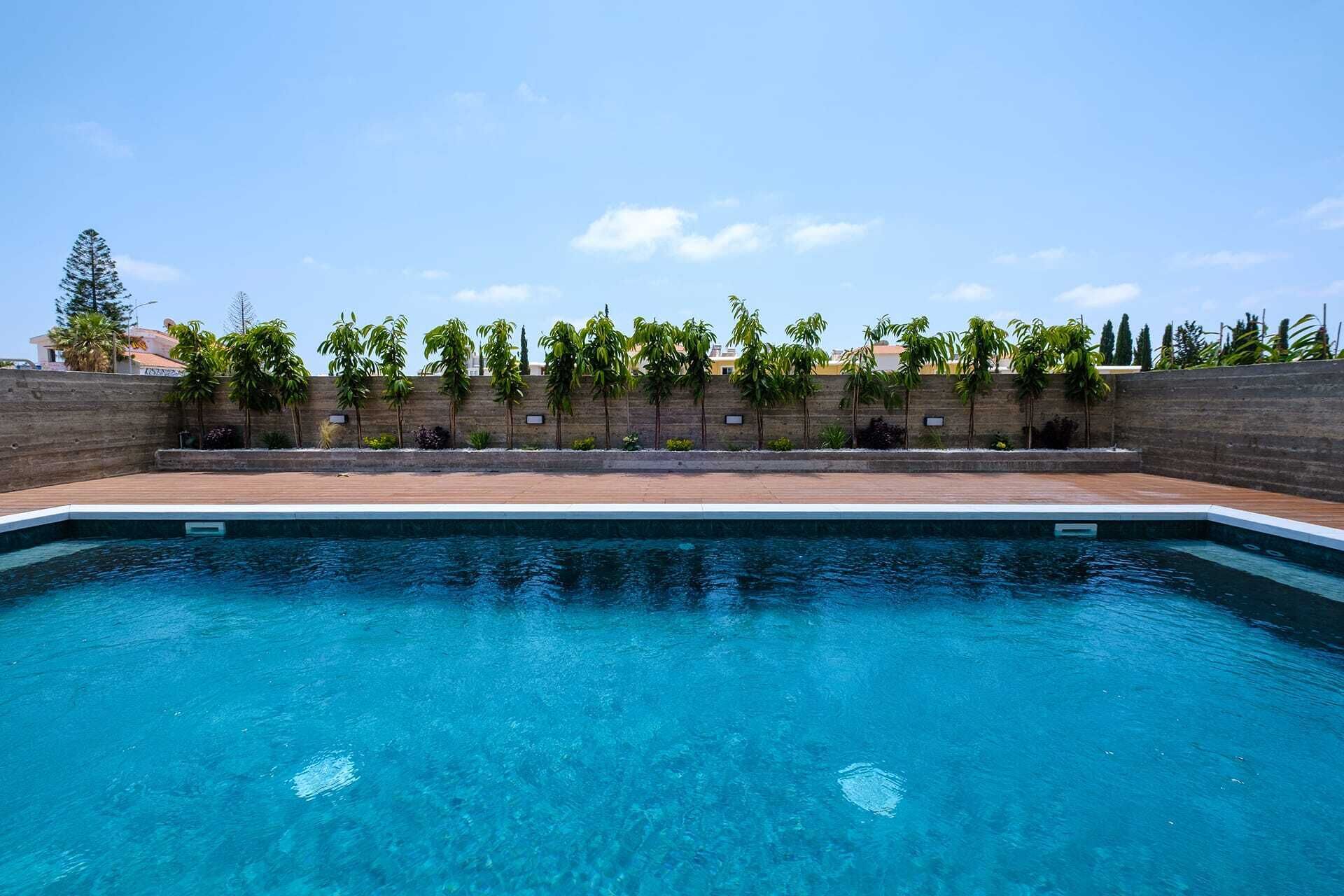 Una piscina con agua azul cristalina, rodeada por un muro de ladrillo y bordeada de diversas plantas.