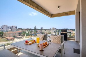 Ein Balkon mit Frühstückstisch, Grill und Blick auf die Stadt.
