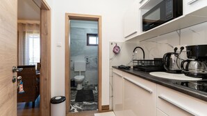 A compact kitchen with a microwave, coffee maker, and kettle, a small sink, and a door leading to a bathroom. - Beachfront apartment 1 - Dramalj by Villas Guide (Crikvenica)