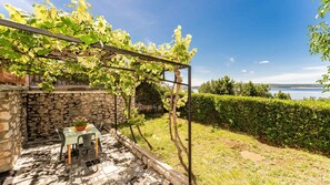 Eine Steinsäule, ein Tisch mit Stühlen und eine Pergola mit Weinlaub.