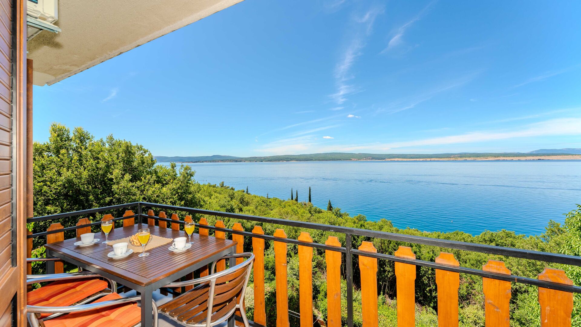 Ein Balkon mit Tisch und Stühlen, mit Blick auf einen See und eine entfernte Uferlinie.