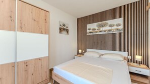 A bedroom with a bed, bedside tables, a wardrobe, and a wall-mounted artwork. - Beachfront apartment 2 - Dramalj by Villas Guide (Crikvenica)