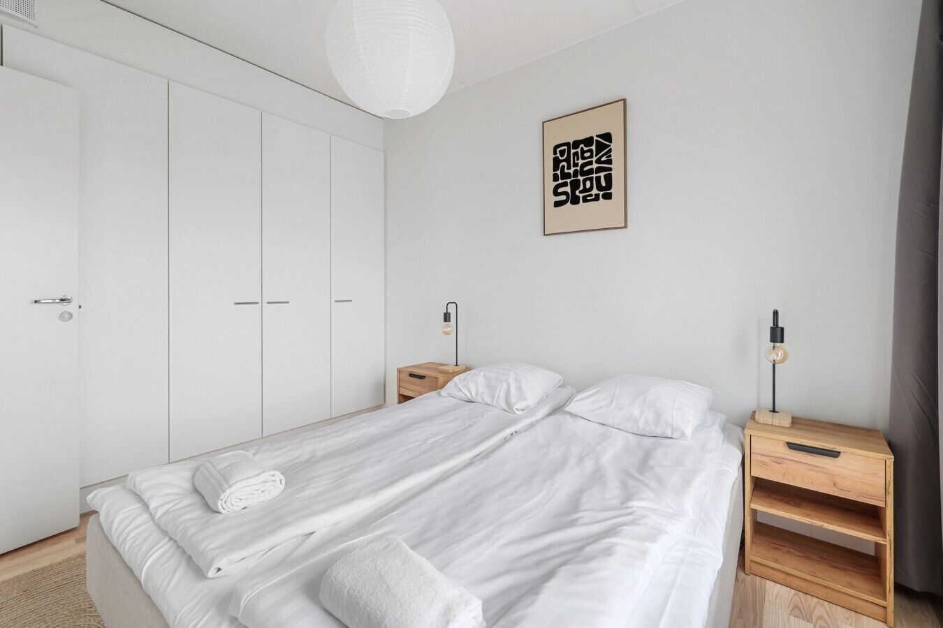 Minimalistinen makuuhuone, jossa on suuri sänky, kaksi yöpöytää ja vaatekaappi.