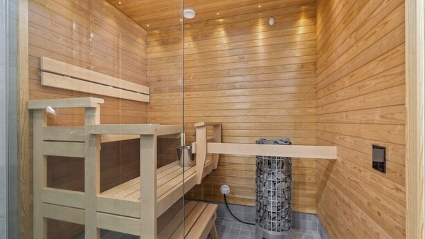 A sauna with wooden walls and benches, a stone heater, and a control panel. - New 2BR Apt with Sauna | Stunning Views | Downtown (Oulu)