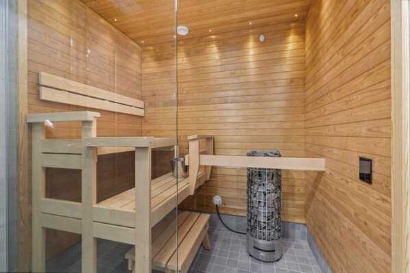 A sauna with wooden walls and benches, a stone heater, and a control panel.