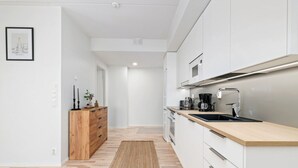 A modern kitchen with white cabinetry, a wooden countertop, and a stainless steel range hood. - New 2BR Apt with Sauna | Stunning Views | Downtown (Oulu)