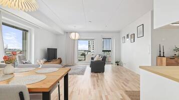 A modern living room with a dining area, large windows, and a view of the cityscape.