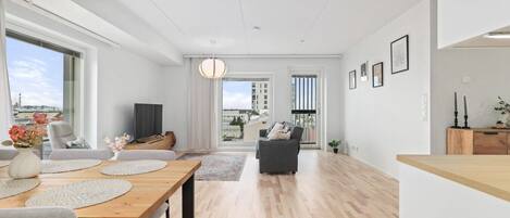 A modern living room with a dining area, large windows, and a view of the cityscape.