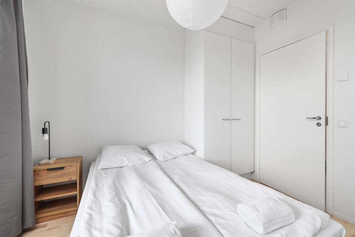 Ett minimalistiskt sovrum med en säng, ett sängbord, en garderob och en hängande lampa.