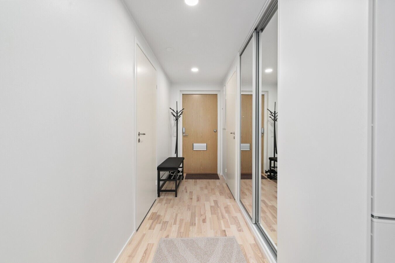 Un pasillo con un banco, piso de madera y una puerta al final.