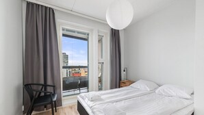 A bedroom with a bed, a chair, a nightstand, and a window with curtains. - New 2BR Apt with Sauna | Stunning Views | Downtown (Oulu)