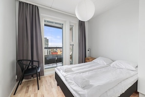 A bedroom with a bed, a chair, a nightstand, and a window with curtains.