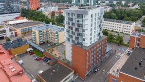 A multi-story building with a modern architectural design, featuring a mix of balconies and windows, surrounded by other buildings and a parking area. - New 2BR Apt with Sauna | Stunning Views | Downtown (Oulu)
