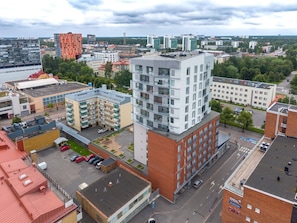 A multi-story building with a modern architectural design, featuring a mix of balconies and windows, surrounded by other buildings and a parking area.