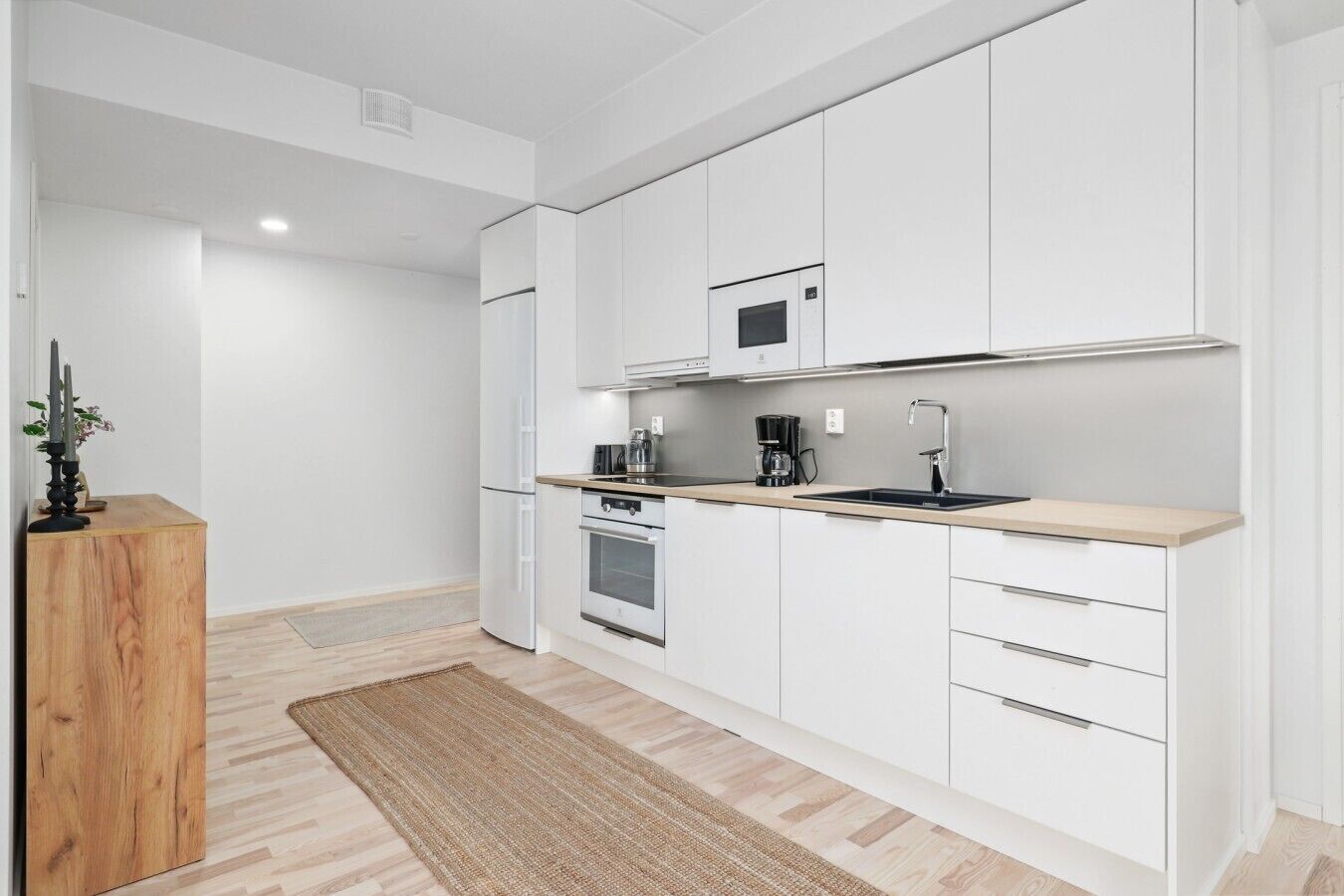 Una cocina moderna con armarios blancos, encimera de madera, horno empotrado y microondas.