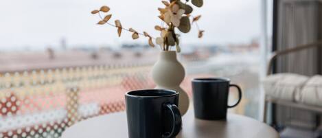 A round table with two black mugs and a white vase with dried flowers.