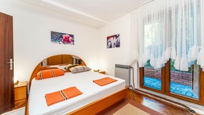 Un dormitorio con una cama, dos mesitas de noche, un radiador y una ventana con cortinas.