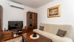Una sala de estar con televisor, aparador de madera, sofá y un cuadro en la pared.