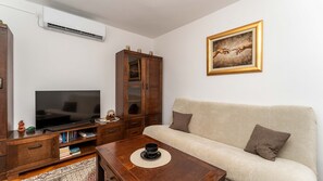 Ein Wohnzimmer mit Fernseher, Holzschrank, Sofa und einem Gemälde an der Wand.