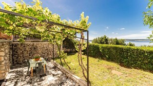Kivimuuri, pöytä tuoleineen ja viiniköynnöksillä koristeltu pergola.