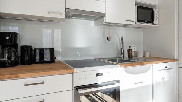 A modern kitchen with white cabinetry, a built-in microwave, a coffee maker, a toaster, and a dishwasher. - Main Square Studio with Free Parking (Tampere)