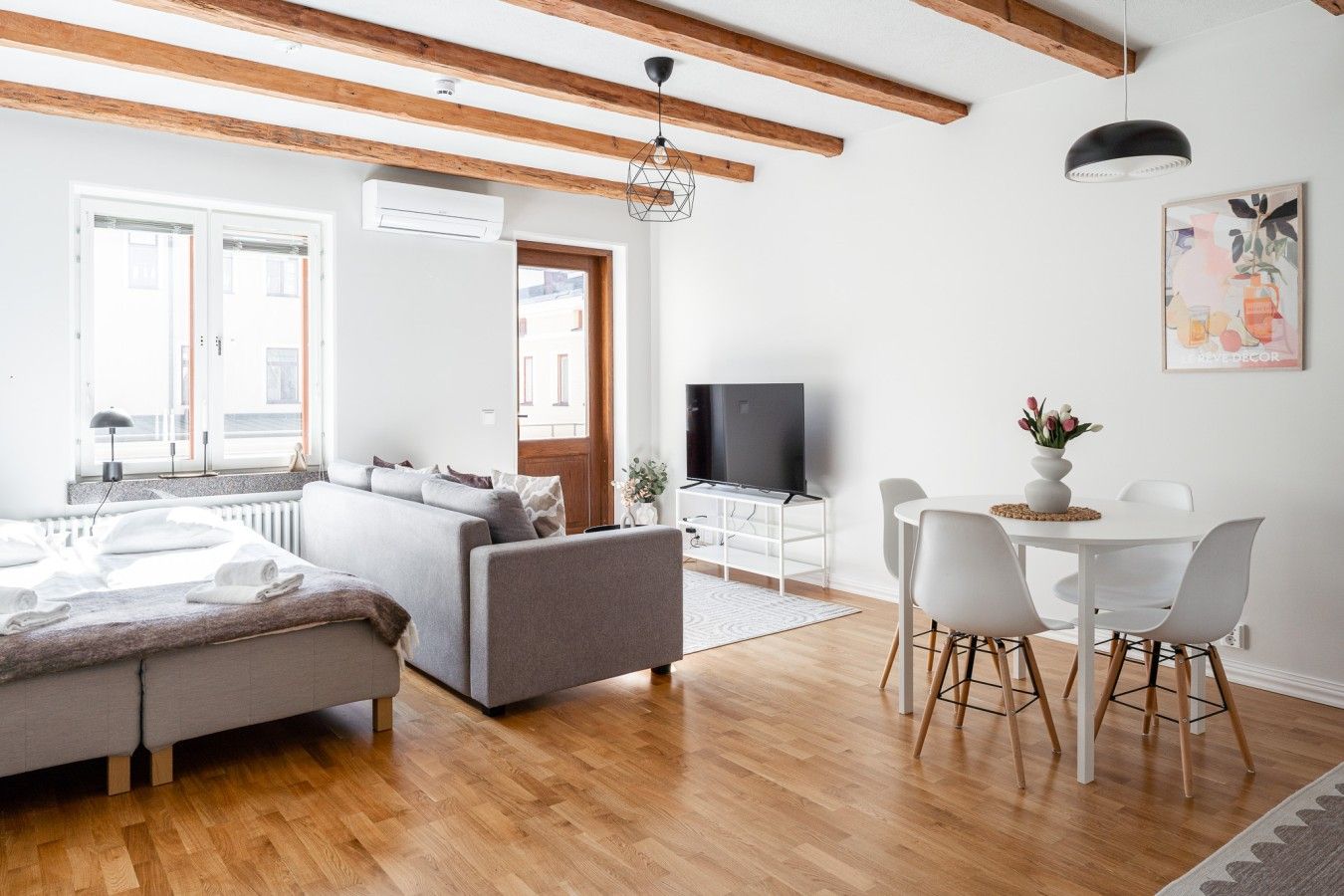 Una sala de estar moderna con un sofá, una mesa de comedor con sillas, un televisor y una ventana con persianas.