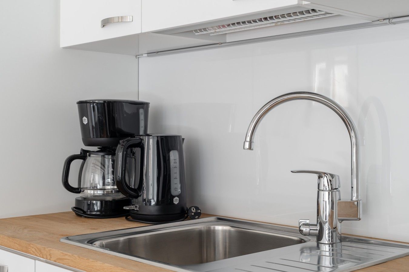 Une cuisine équipée d’un évier en acier inoxydable, d’un robinet moderne et de deux machines à café noires posées sur le plan de travail.