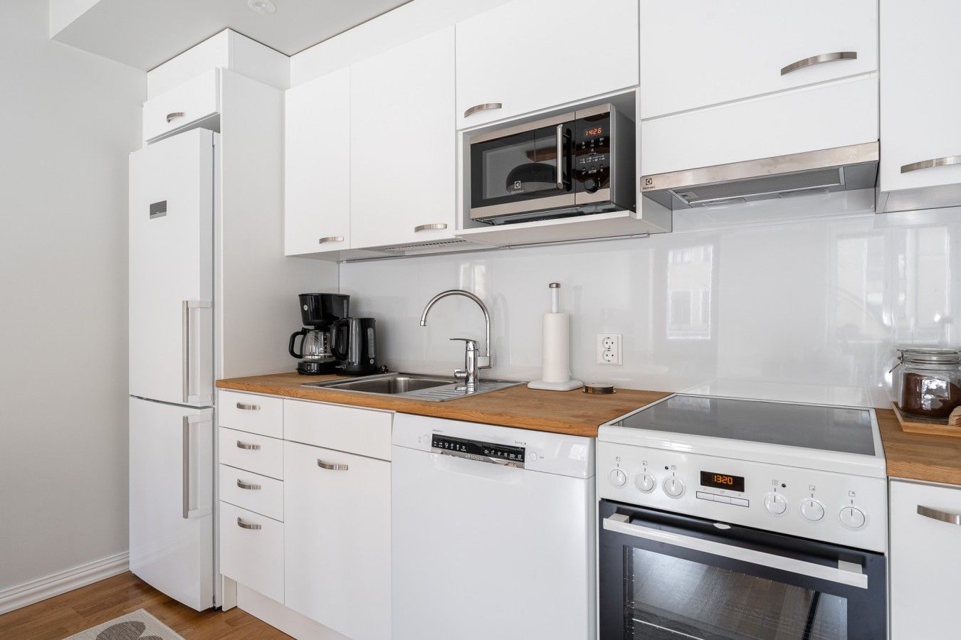 A modern kitchen with white cabinetry, a built-in microwave, a coffee maker, and a dishwasher.
