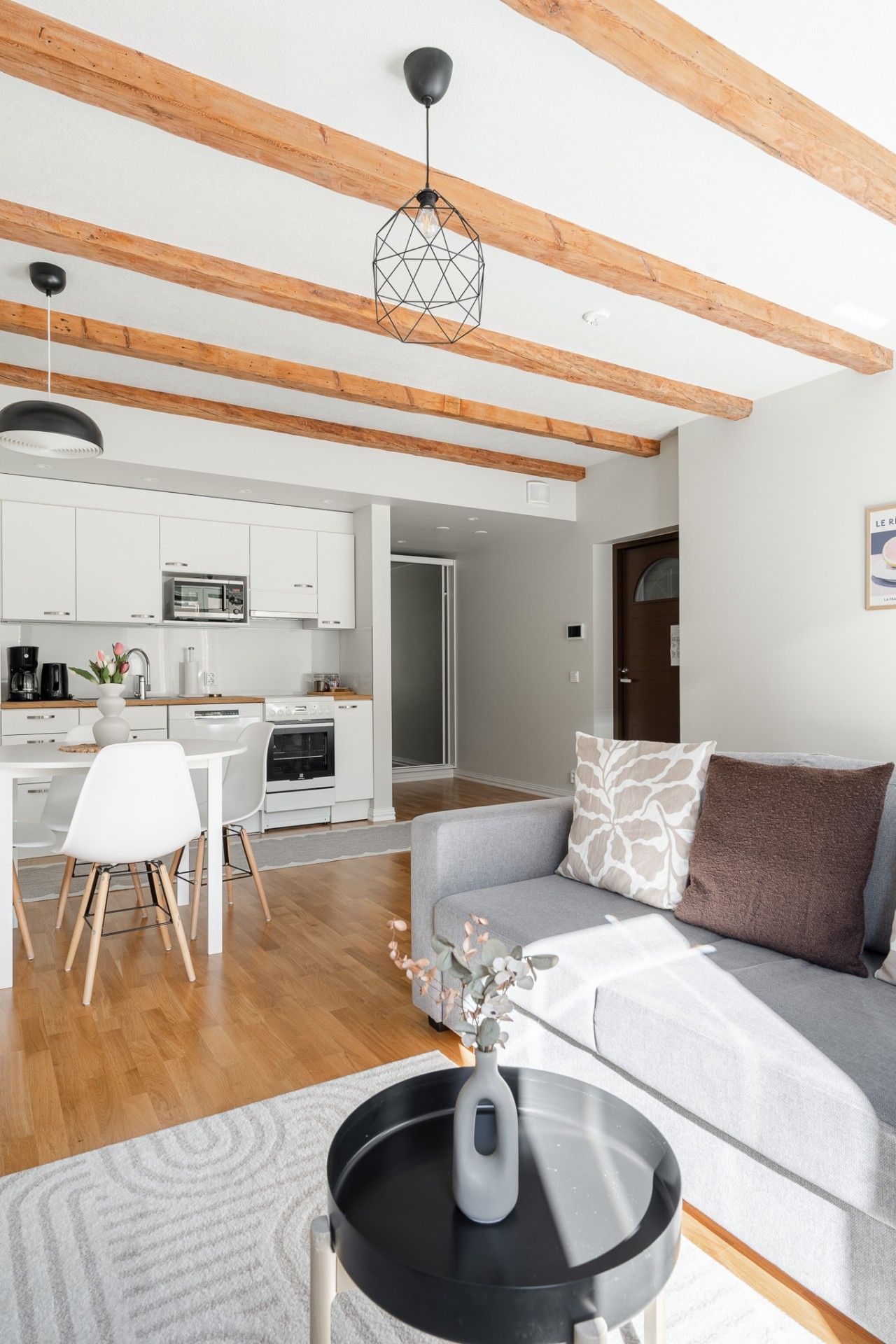 Een moderne woonruimte met een keuken, eethoek en een bank met decoratieve kussens.