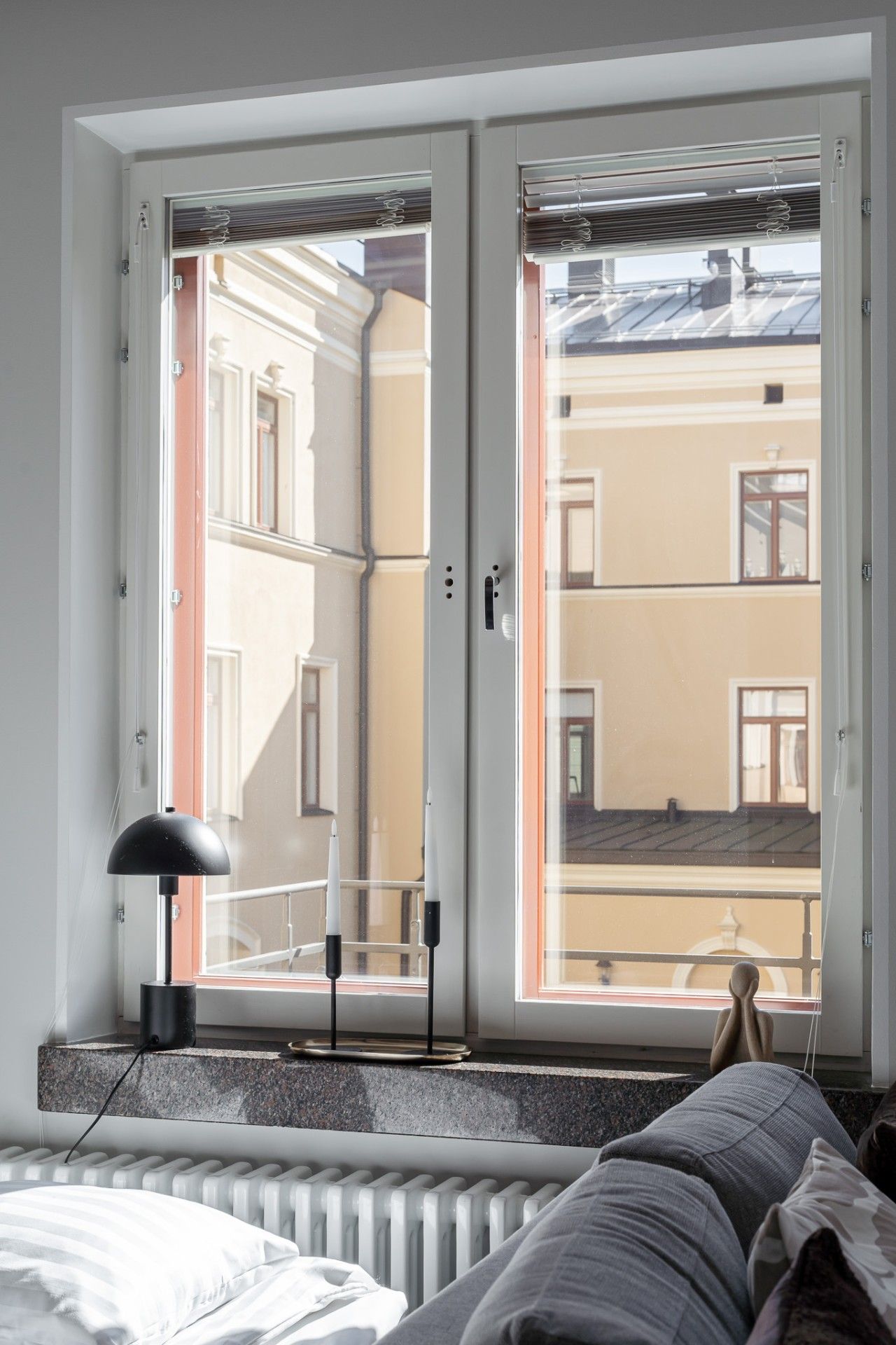 Una habitación con cama, un radiador, una ventana con persianas y vistas a un edificio.