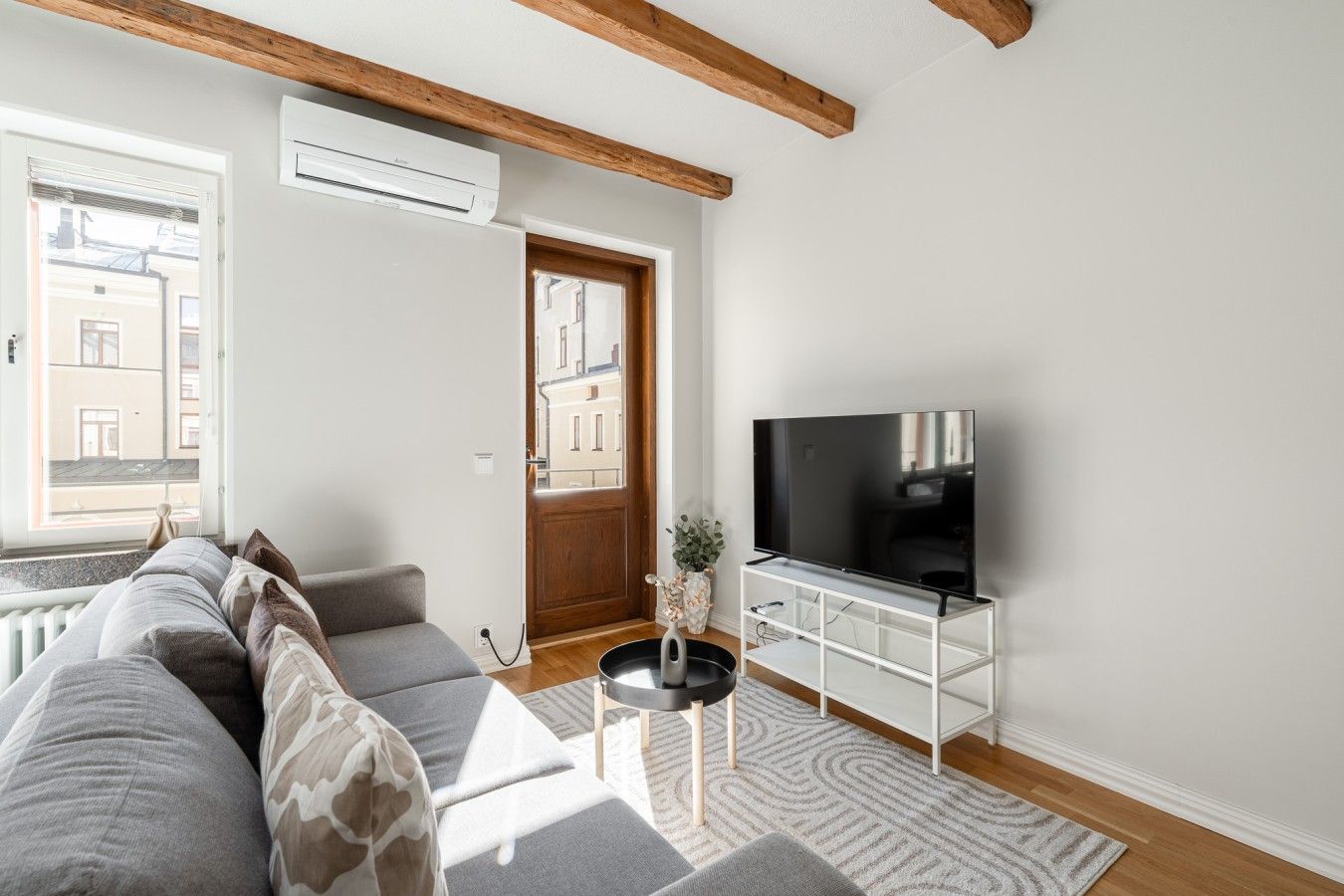 Un salon moderne avec un canapé, un téléviseur posé sur un meuble et une porte donnant sur l’extérieur.