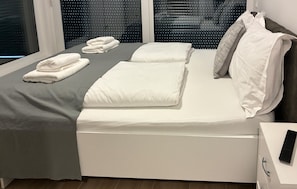 A neatly made bed with white linens and pillows, a grey blanket, and a folded towel on the side. - Lovely home in Milcetici (Milcetici)