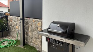 Ein Grillplatz im Freien mit Bedienfeld, Steinwand und Gartenschlauch.