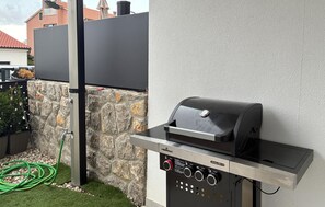 Ein Grillplatz im Freien mit Bedienfeld, Steinwand und Gartenschlauch.