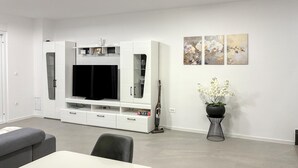 Ein modernes Wohnzimmer mit Fernseher, Esstisch und einer Zimmerpflanze.