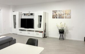 Ein modernes Wohnzimmer mit Fernseher, Esstisch und einer Zimmerpflanze.