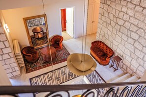 Une pièce aux hauts plafonds, dotée d’un sol à motifs, d’un grand miroir et d’un coin salon avec un canapé et des fauteuils.
