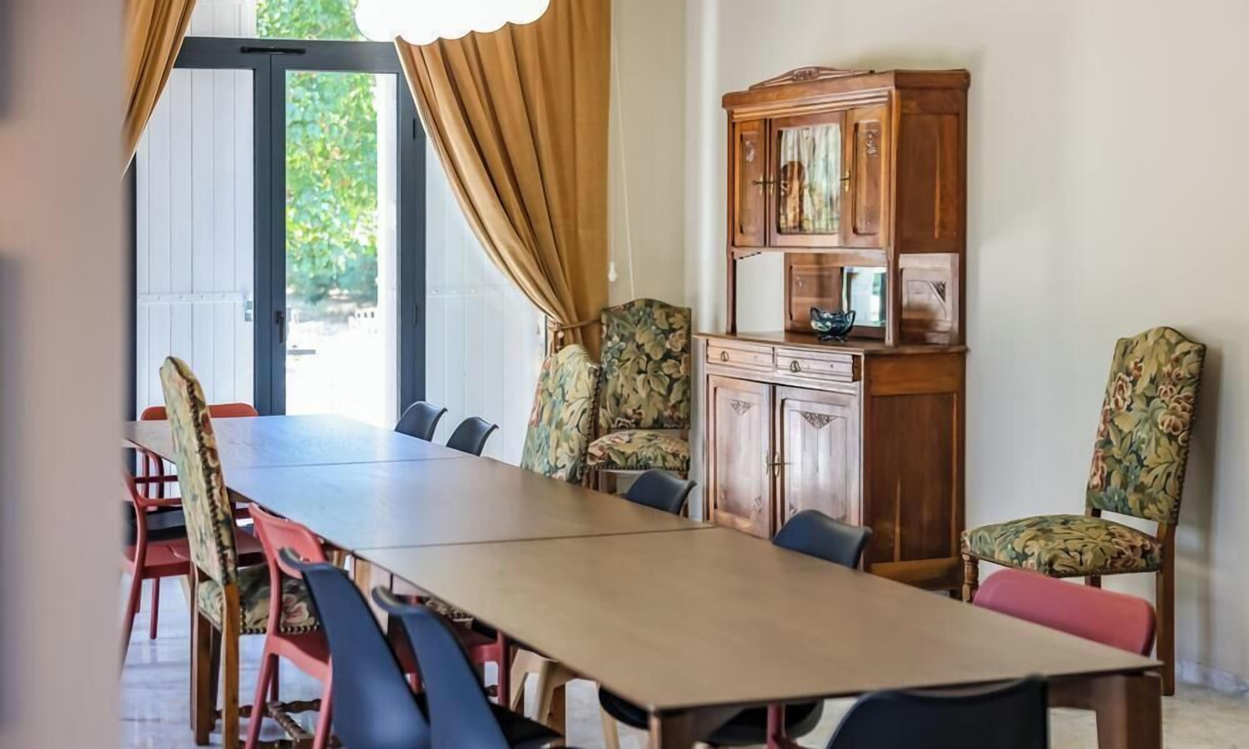 Une salle de conférence avec une longue table, des chaises, un buffet et une vue sur l’extérieur, visible à travers une porte.