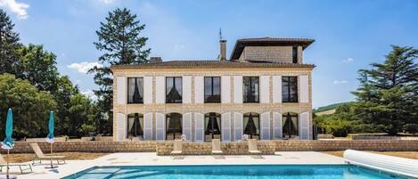 A two-story stone building with a swimming pool in front.