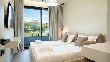 A hotel room with a bed, two bedside tables, a TV, and a view of the outside.