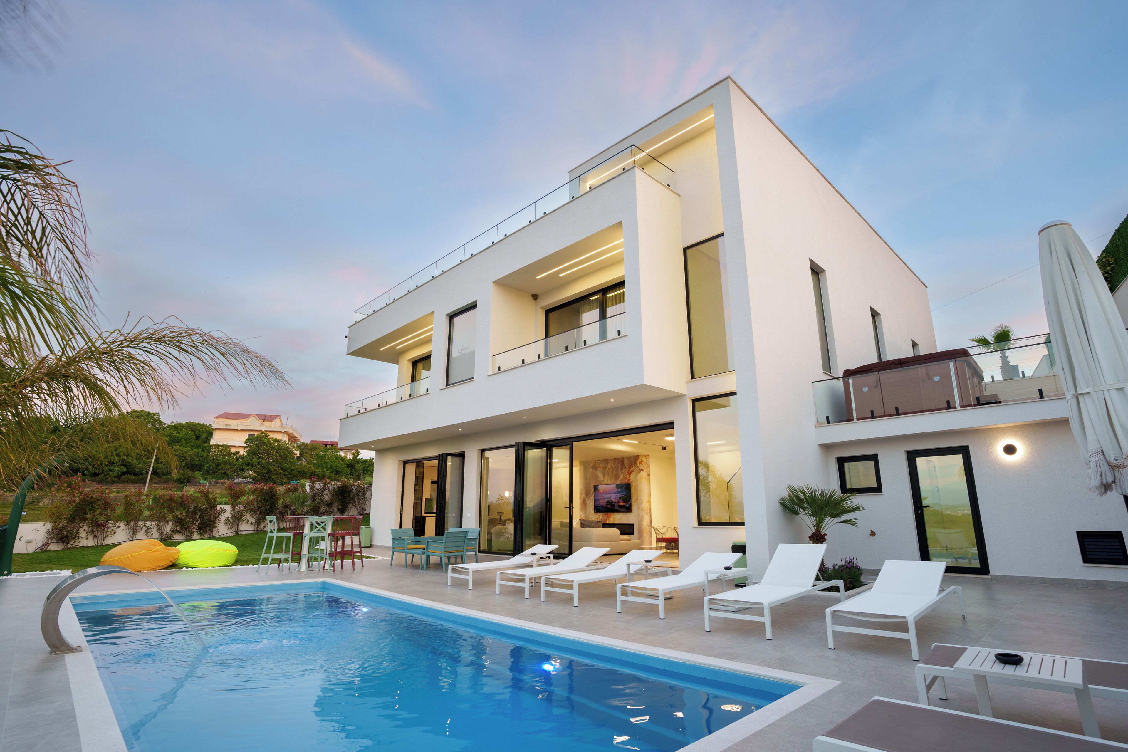 A modern two-story house with a swimming pool, outdoor seating, and a balcony.