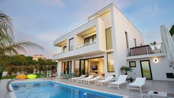 A modern two-story house with a swimming pool, outdoor seating, and a balcony.